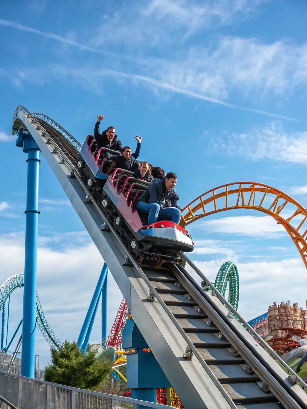 A high-angle, vibrant photograph capturing the full scale and speed of the Hyperion roller coaster at Energyland, with riders visible and expressing excitement. The background shows a clear blue sky and the park's landscape.